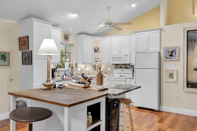 kitchen featuring butcher block counters, a breakfast bar area, white cabinetry, vaulted ceiling, and white appliances