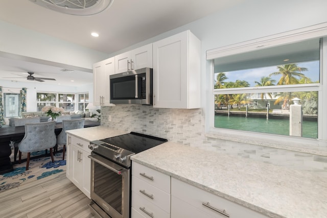 kitchen with white cabinets, backsplash, stainless steel appliances, light stone countertops, and a water view