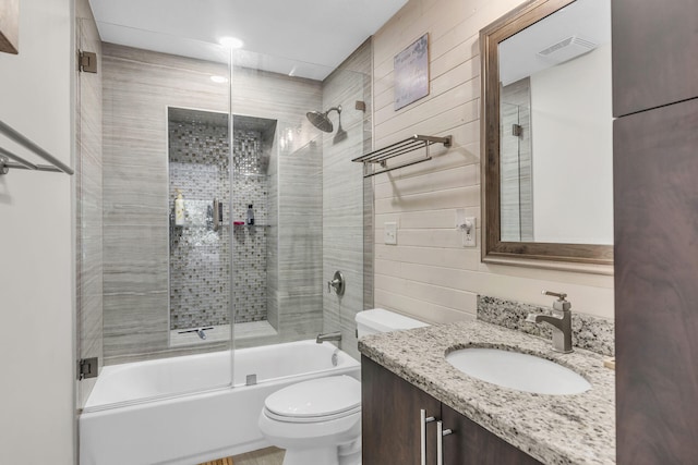 full bathroom featuring vanity, wooden walls, toilet, and combined bath / shower with glass door