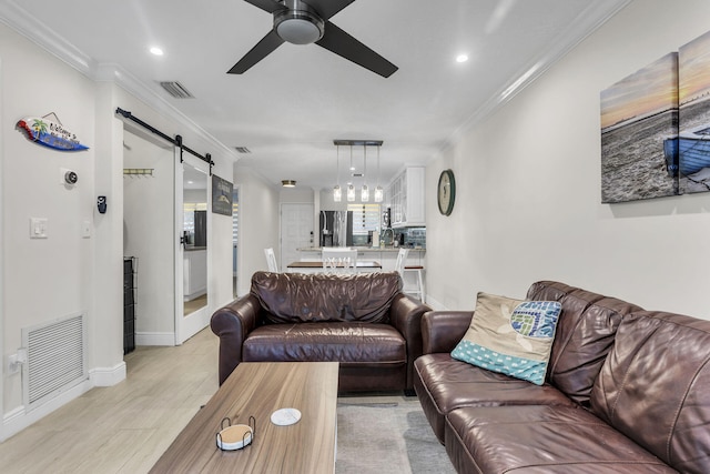 living room featuring light hardwood / wood-style flooring, ornamental molding, a barn door, and ceiling fan