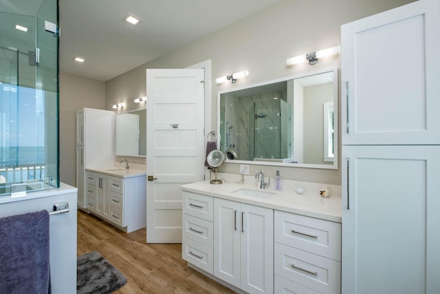 bathroom with two vanities, a sink, a shower stall, and wood finished floors