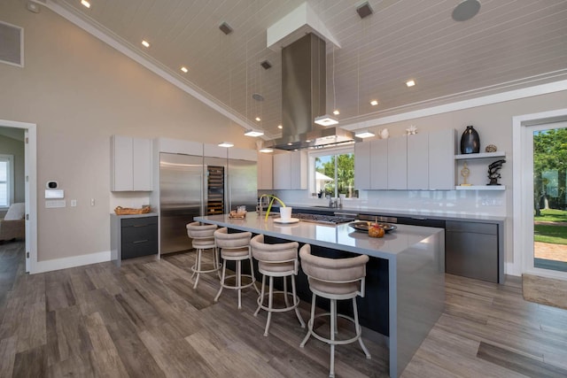 kitchen with a kitchen island with sink, island range hood, white cabinetry, light countertops, and open shelves