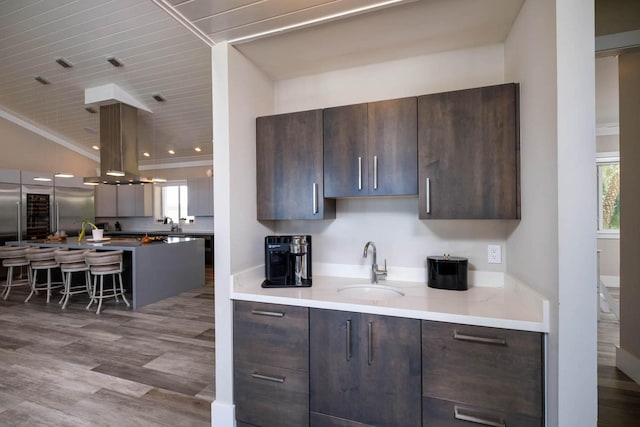 kitchen featuring modern cabinets, wood finished floors, stainless steel built in fridge, island exhaust hood, and a sink