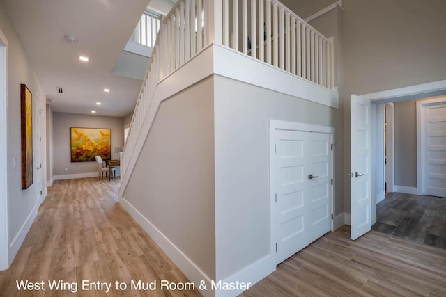 hall featuring a towering ceiling and light hardwood / wood-style flooring