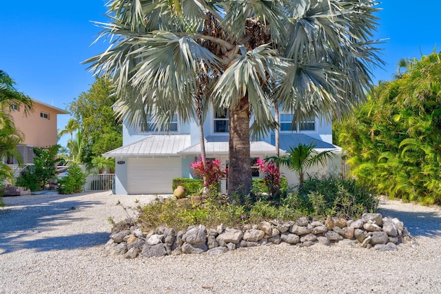 view of property hidden behind natural elements featuring a gate, fence, gravel driveway, stucco siding, and metal roof