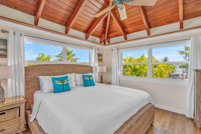 bedroom with baseboards, multiple windows, light wood-style floors, and vaulted ceiling with beams