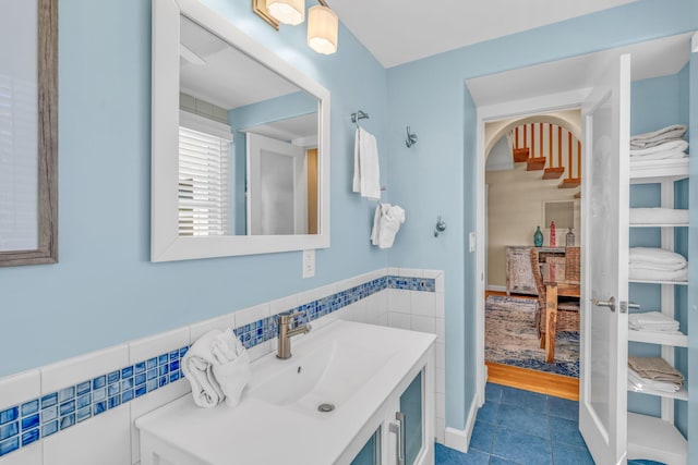 bathroom featuring tile patterned flooring, tile walls, vanity, and wainscoting