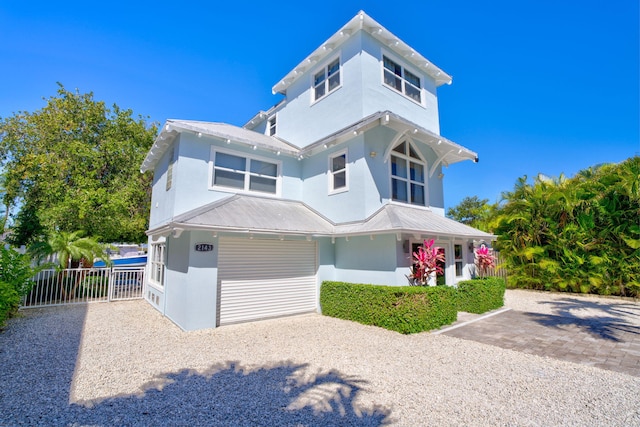 view of front of house featuring metal roof, gravel driveway, stucco siding, and fence