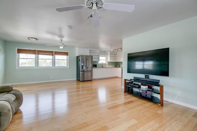 living room featuring ceiling fan, light wood-style flooring, and baseboards