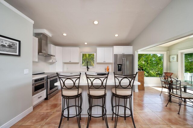 kitchen with wall chimney exhaust hood, white cabinetry, appliances with stainless steel finishes, plenty of natural light, and a kitchen island