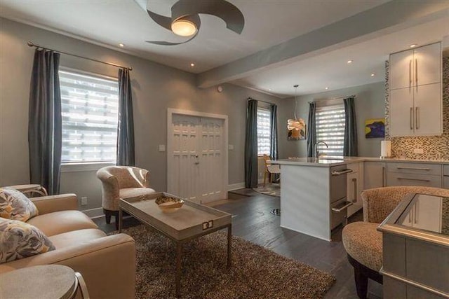 living room featuring beamed ceiling, dark wood-type flooring, sink, and ceiling fan