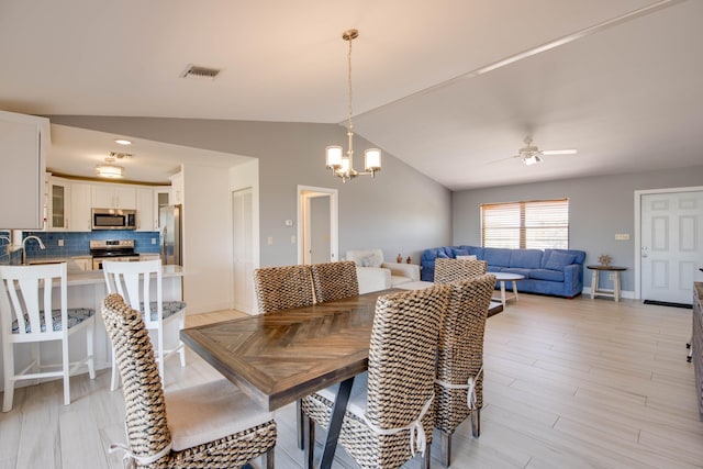 dining room with lofted ceiling, sink, ceiling fan with notable chandelier, and light wood-type flooring