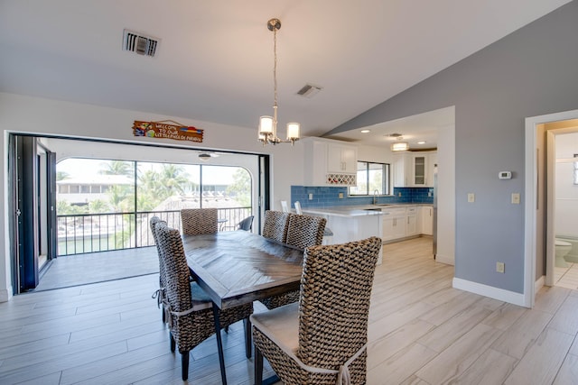 dining space with lofted ceiling, sink, a notable chandelier, and light hardwood / wood-style floors