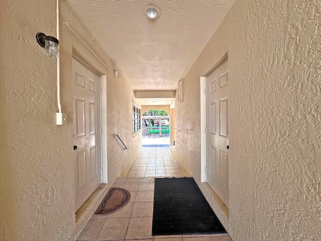 hall featuring a textured wall, tile patterned floors, and a textured ceiling