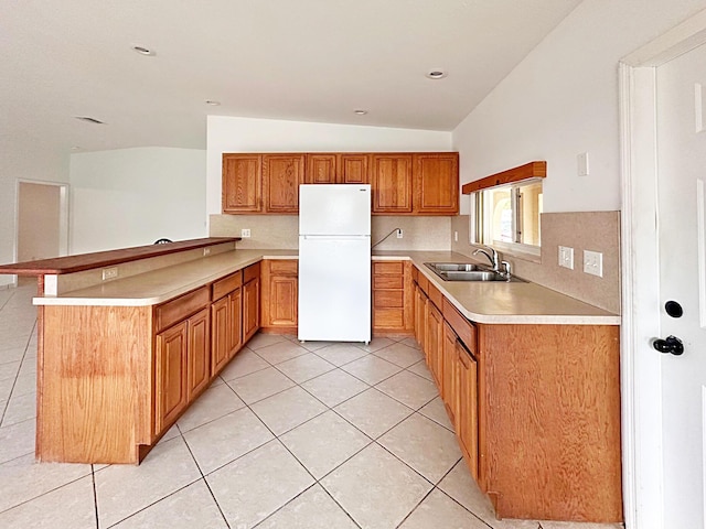 kitchen featuring freestanding refrigerator, a sink, vaulted ceiling, a peninsula, and light tile patterned floors