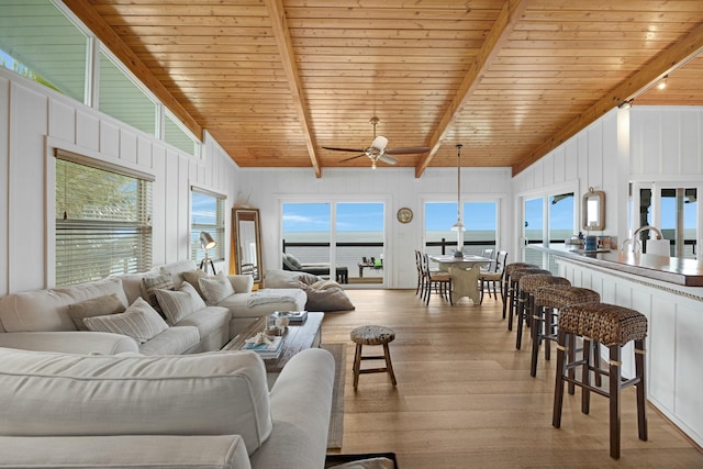 living room featuring beamed ceiling, ceiling fan, light hardwood / wood-style floors, a water view, and wooden ceiling