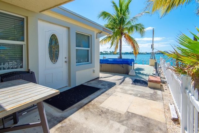 doorway to property with a patio area, a hot tub, and a water view