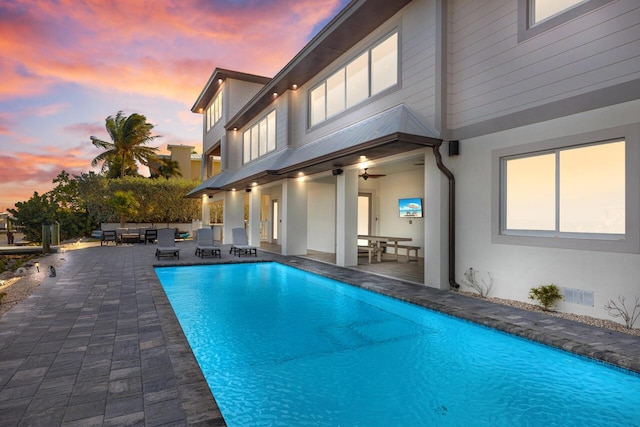 pool at dusk with an outdoor hangout area, a patio, and ceiling fan