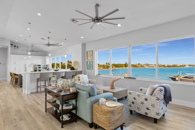 living room with ceiling fan, a water view, and light hardwood / wood-style floors