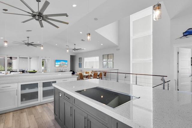 kitchen featuring hanging light fixtures, plenty of natural light, black electric stovetop, and light stone counters