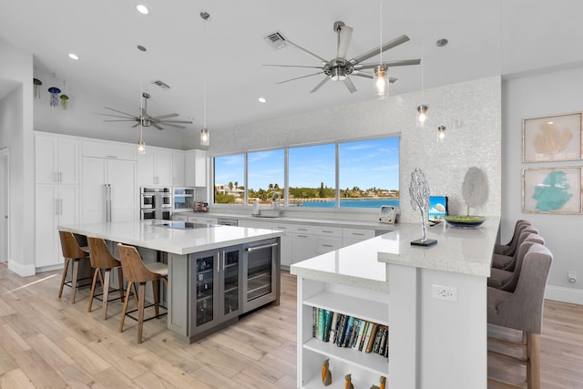 kitchen with hanging light fixtures, a kitchen breakfast bar, white cabinets, a center island with sink, and beverage cooler