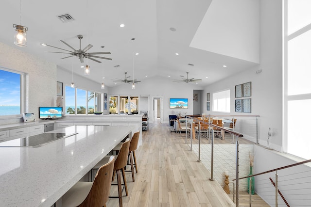 kitchen with hanging light fixtures, light hardwood / wood-style flooring, black electric cooktop, a kitchen breakfast bar, and light stone countertops