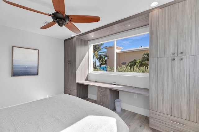 bedroom featuring built in desk, light hardwood / wood-style floors, and ceiling fan