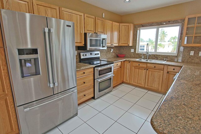 kitchen featuring sink, light tile patterned floors, appliances with stainless steel finishes, dark stone countertops, and tasteful backsplash