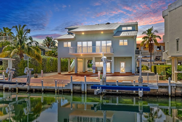 back house at dusk featuring a water view, a balcony, and a patio area