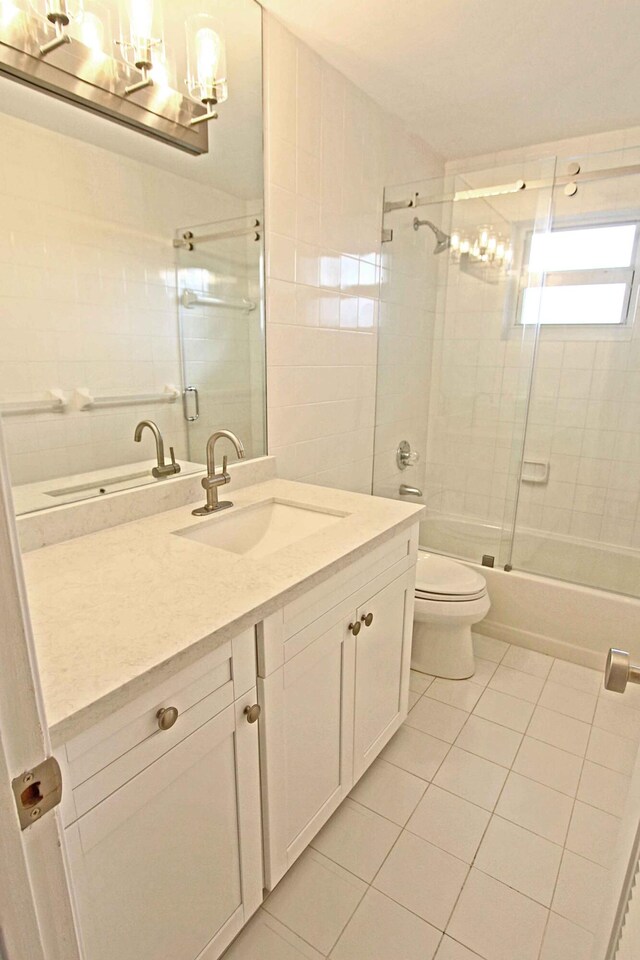 full bathroom with tile patterned flooring, bath / shower combo with glass door, vanity, and toilet