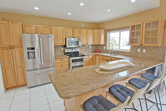 kitchen featuring sink, stainless steel appliances, a kitchen breakfast bar, light stone counters, and kitchen peninsula