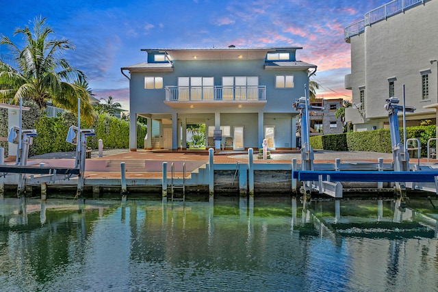 back house at dusk with a water view and a balcony