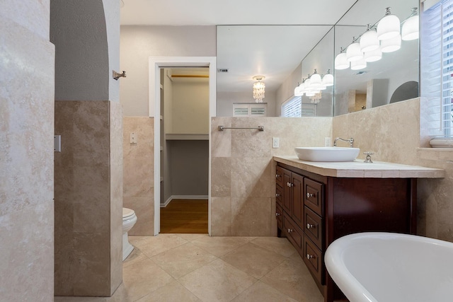 bathroom featuring tile patterned floors, toilet, tile walls, vanity, and a washtub