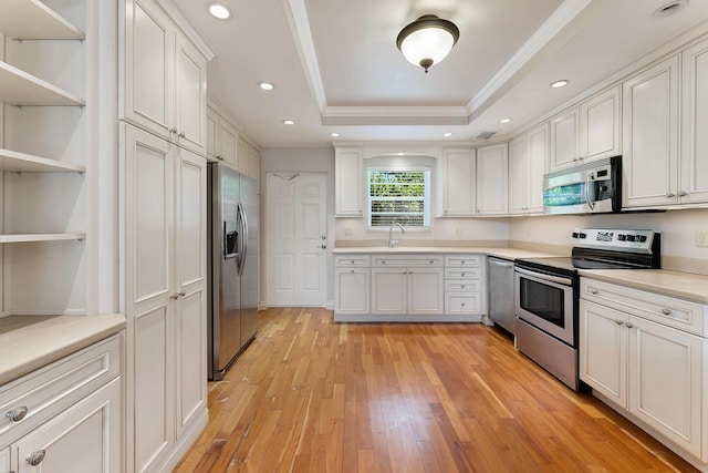 kitchen with sink, white cabinetry, light wood-type flooring, appliances with stainless steel finishes, and a tray ceiling