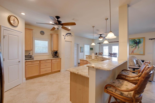 kitchen featuring a breakfast bar, light brown cabinetry, hanging light fixtures, kitchen peninsula, and light stone countertops