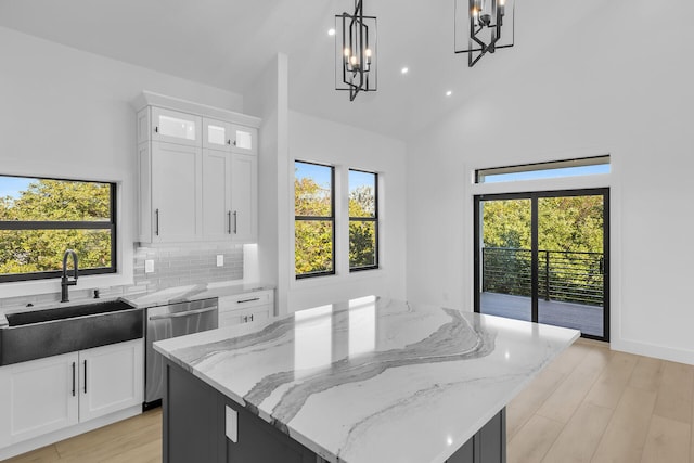 kitchen featuring light stone counters, light wood-style floors, a kitchen island, a sink, and dishwasher