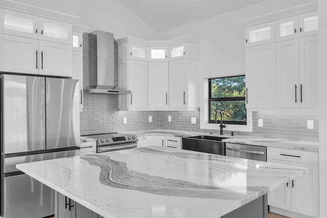 kitchen featuring stainless steel appliances, a kitchen island, a sink, white cabinets, and wall chimney range hood