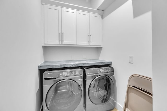 clothes washing area with washer and clothes dryer, cabinet space, and baseboards