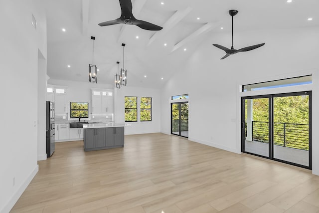 unfurnished living room with light wood-style floors, baseboards, high vaulted ceiling, and a sink