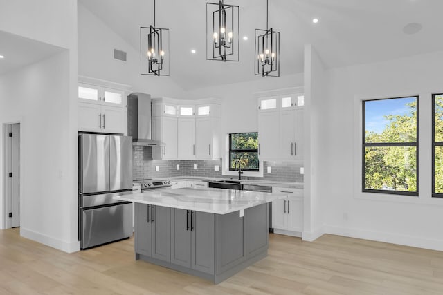 kitchen featuring high vaulted ceiling, stainless steel appliances, white cabinetry, wall chimney range hood, and a center island