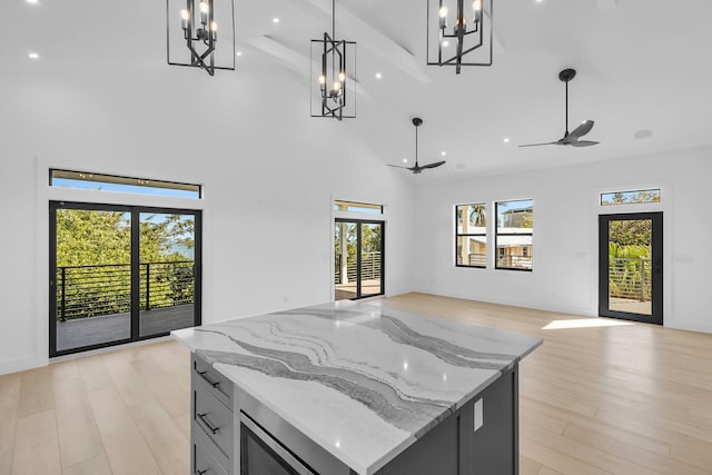 kitchen featuring a towering ceiling, light wood-style floors, open floor plan, hanging light fixtures, and light stone countertops