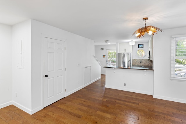 kitchen with stainless steel fridge, a breakfast bar area, white cabinets, decorative light fixtures, and kitchen peninsula