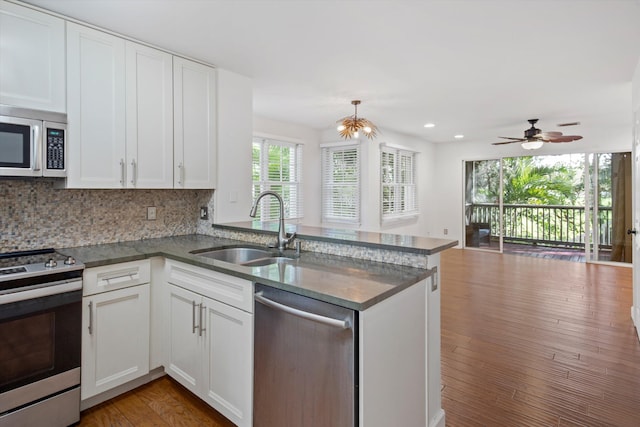 kitchen with sink, hardwood / wood-style flooring, stainless steel appliances, white cabinets, and kitchen peninsula