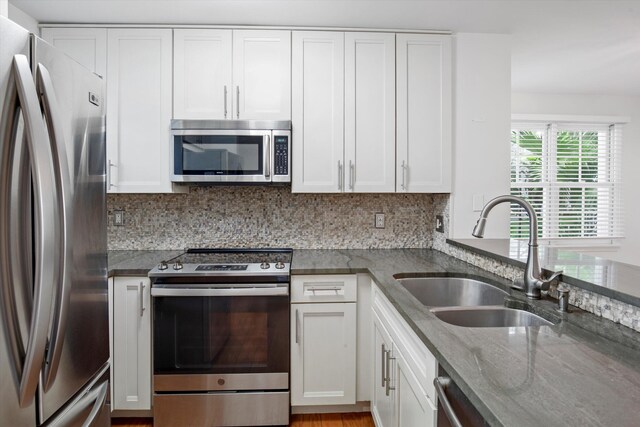 kitchen with white cabinetry, appliances with stainless steel finishes, sink, and dark stone counters