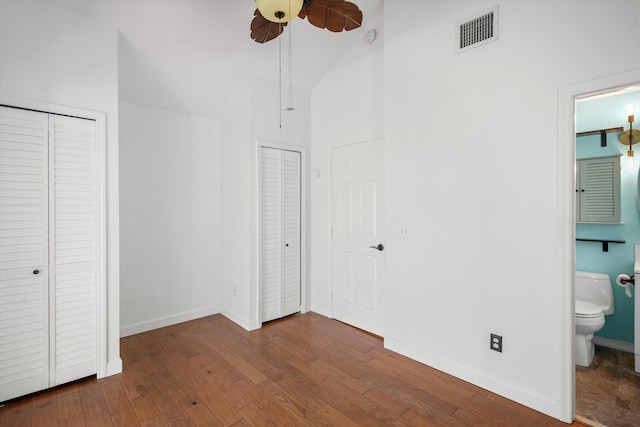 unfurnished bedroom with ensuite bathroom, multiple closets, ceiling fan, dark hardwood / wood-style flooring, and a towering ceiling