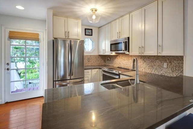 kitchen featuring sink, white cabinetry, appliances with stainless steel finishes, kitchen peninsula, and dark stone counters