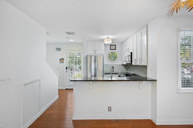 kitchen with stainless steel appliances, tasteful backsplash, white cabinets, a kitchen bar, and kitchen peninsula