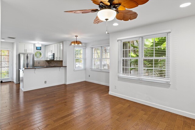 unfurnished living room featuring ceiling fan, a healthy amount of sunlight, and dark hardwood / wood-style floors