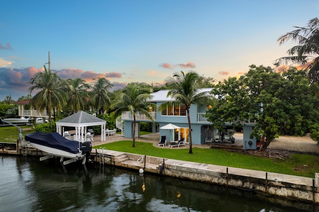 dock area featuring a balcony, a water view, and a lawn