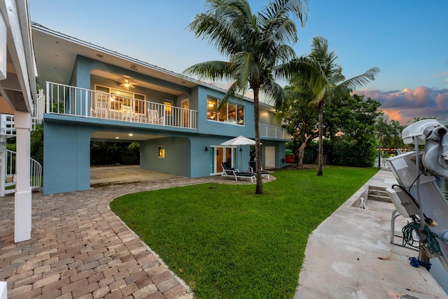 back house at dusk with a balcony, a yard, and a patio area